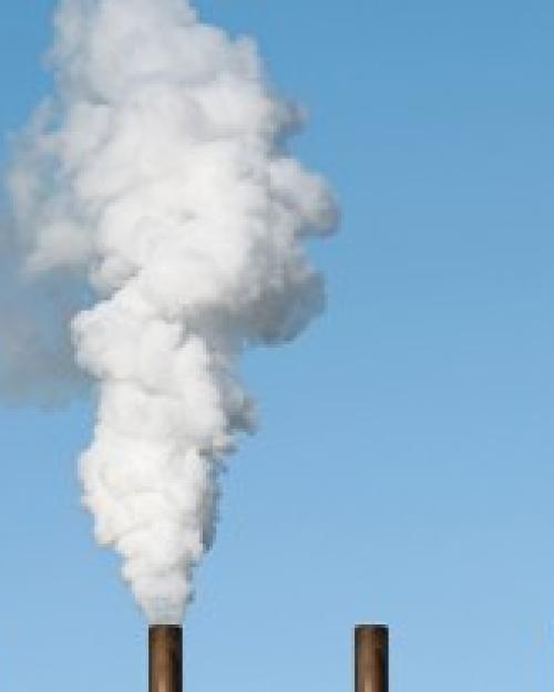 five smoke stacks against a blue sky; the second from left belches smoke