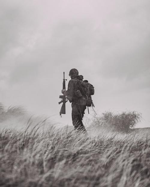 Soldier in uniform with backpack holding rifle walking across grasslands