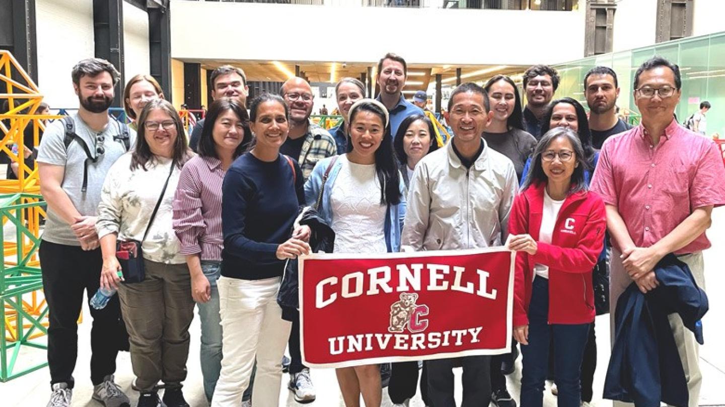 Several people stand together behind a "Cornell University" banner